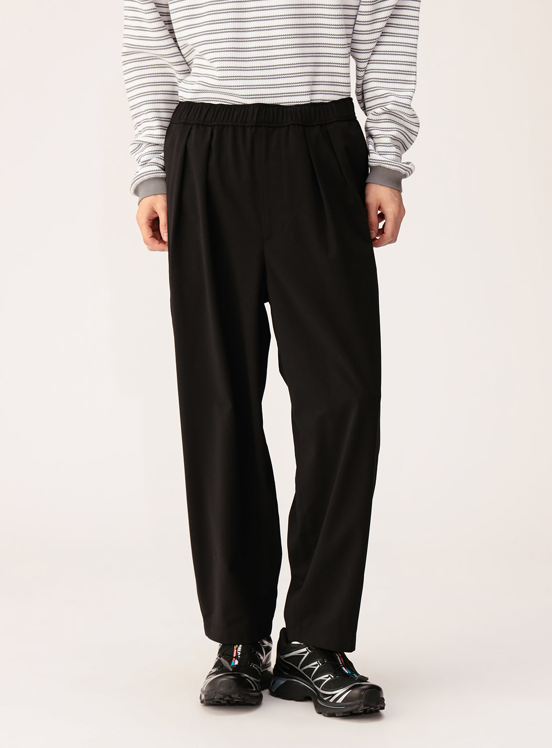 A person wears BEAMS Quick-Dry 2-Pleat Wide Tapered Easy Pants and a gray and white striped long-sleeve shirt with black sneakers, standing against a plain light background. The face is not visible.