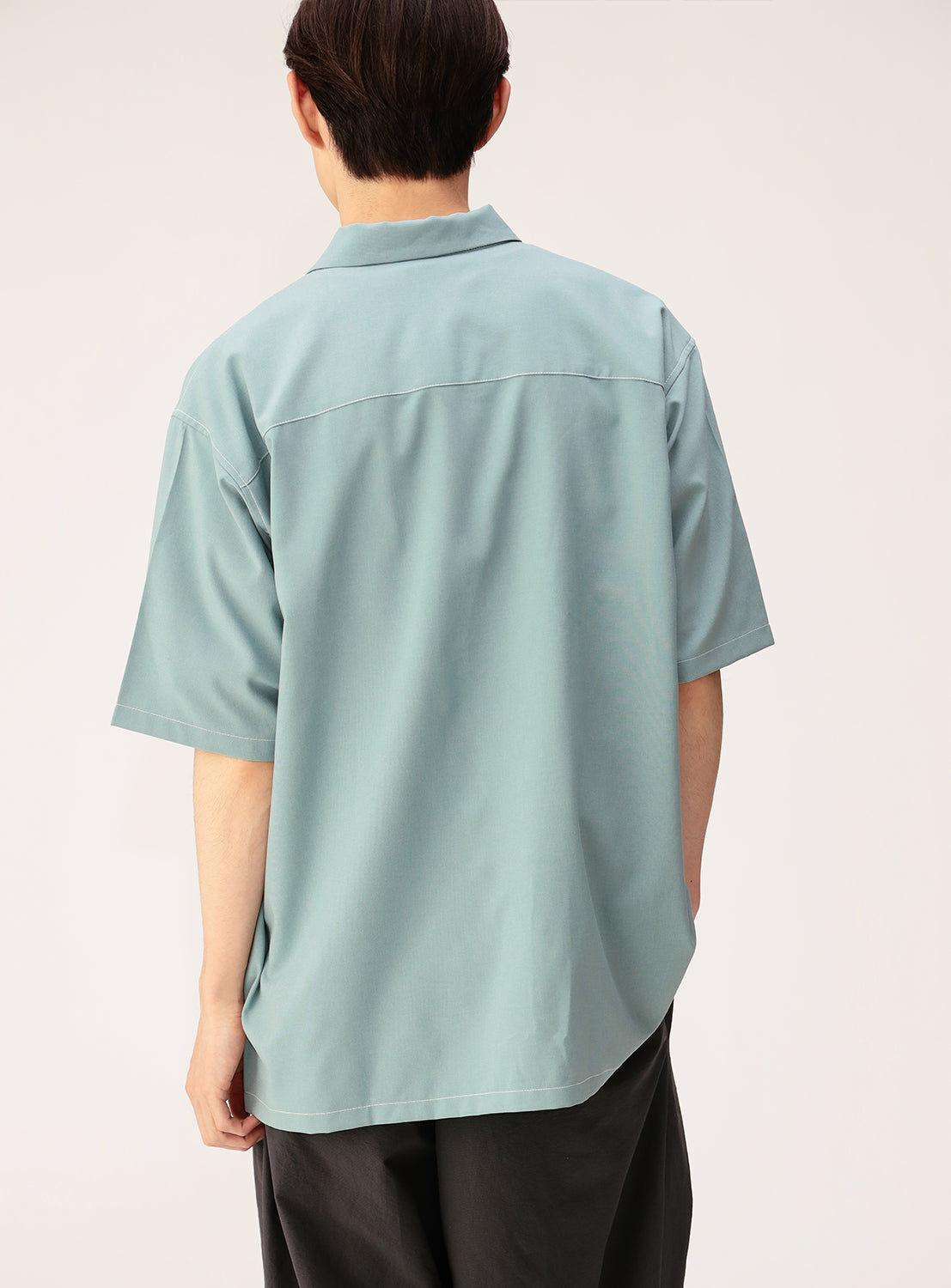A person stands facing away, wearing the BEAMS Wide Fit Double Pocket Contrast Stitch Shirt in light blue, paired with dark pants against a plain background.