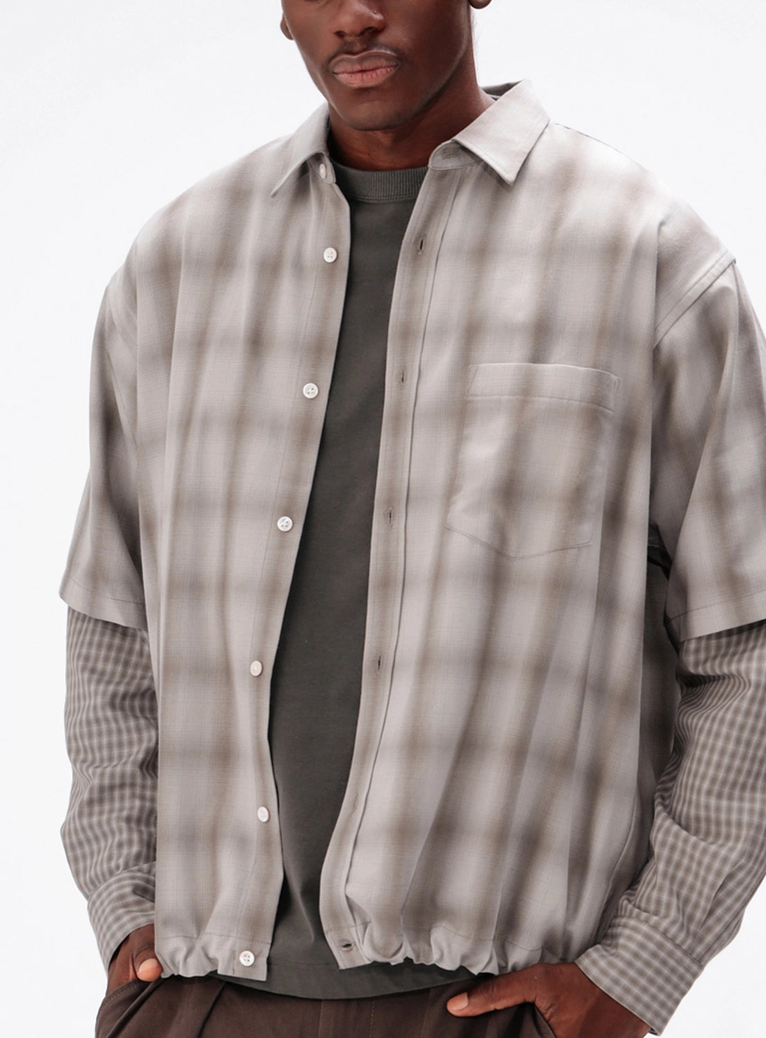 A person wears a BEAMS Layered Check Shirt featuring a wide-fit, short-sleeved plaid shirt worn over a dark long-sleeved shirt.