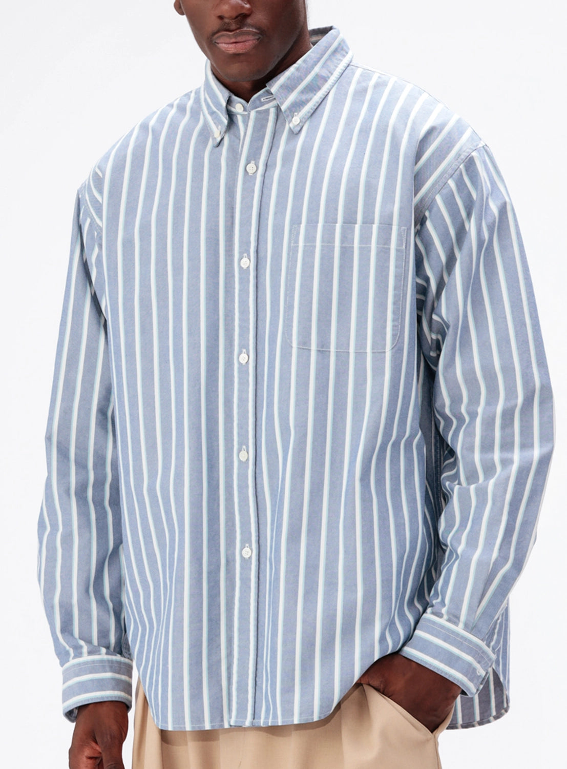 A person wearing a BEAMS Heavy Oxford Button-Down in blue and white vertical stripes, finished with an oversized chest pocket.