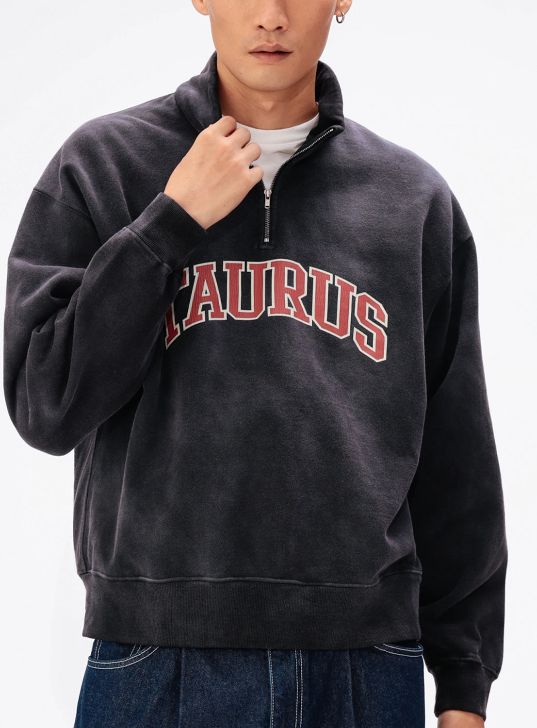 A person wearing a BEAMS Faded Souvenir Half Zip Pullover in faded black with the word TAURUS in red and white varsity lettering on the chest.
