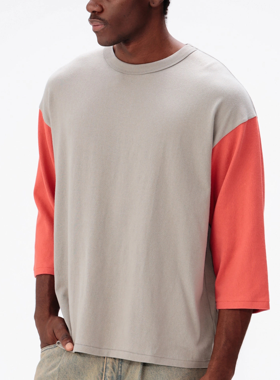 A person wearing a BEAMS Baseball 9/10 Sleeve T-Shirt, a wide-fit, color-blocked top featuring a grey crew-neck and three-quarter length red sleeves.