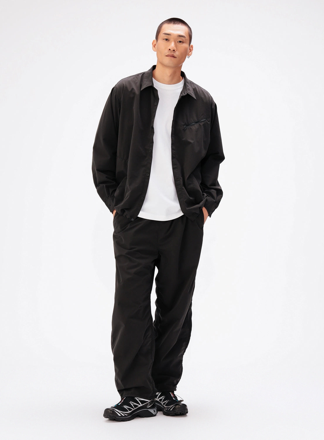 A man wearing a black BEAMS Tech Shirt over a white crew-neck t-shirt with matching black relaxed-fit trousers.