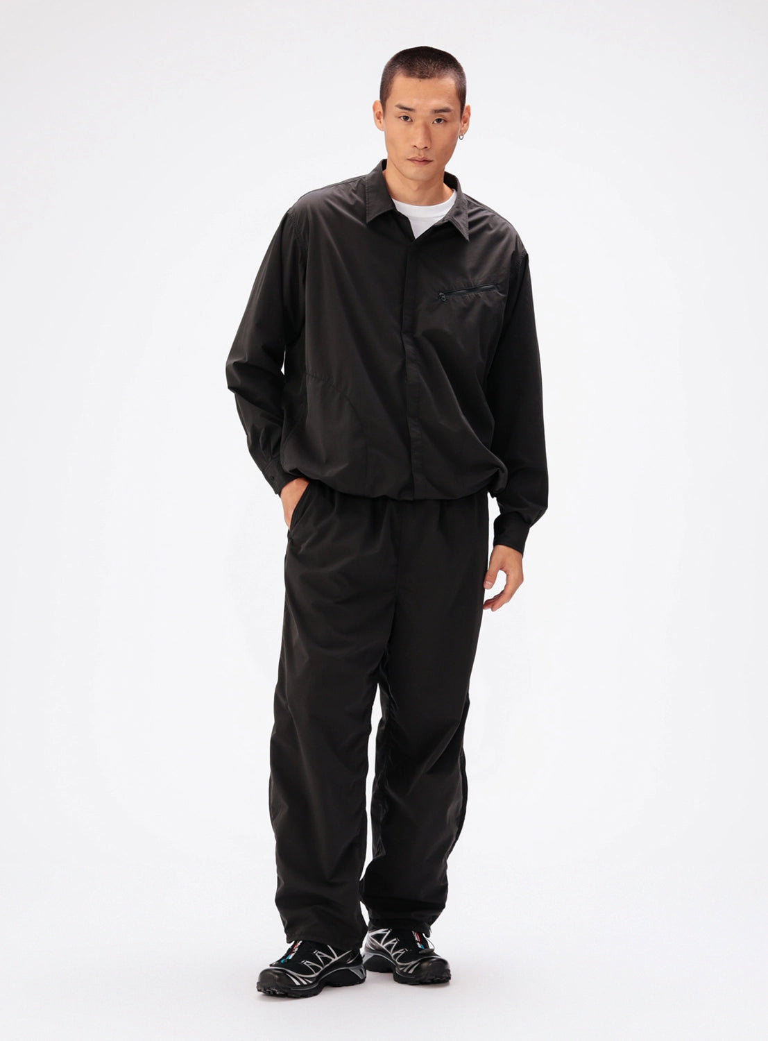 A person wearing a black, water-repellent BEAMS Tech Shirt with long sleeves and matching black trousers.