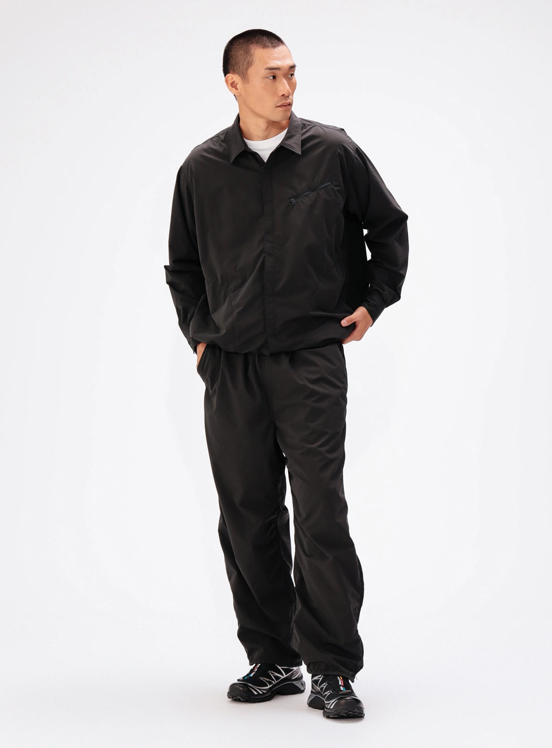 A man wears a black water-repellent, long-sleeved BEAMS Tech Shirt with matching relaxed-fit trousers.
