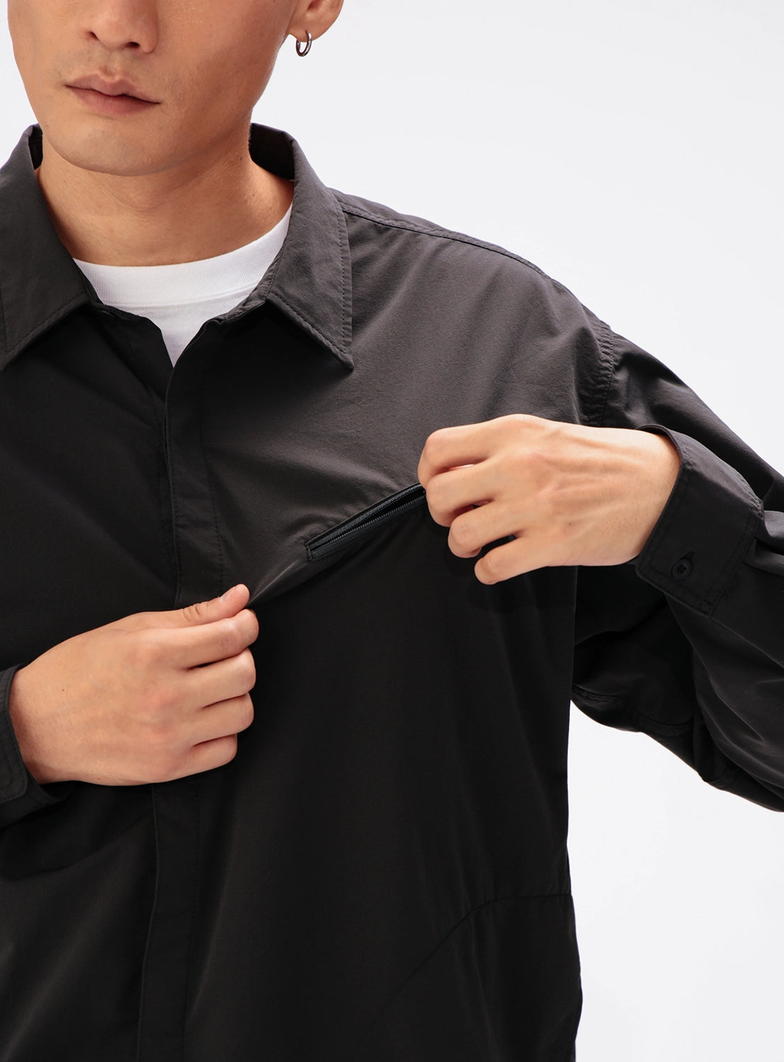 A person wearing a black BEAMS Tech Shirt, a stretch fabric button-down with a zippered chest pocket that they are opening.