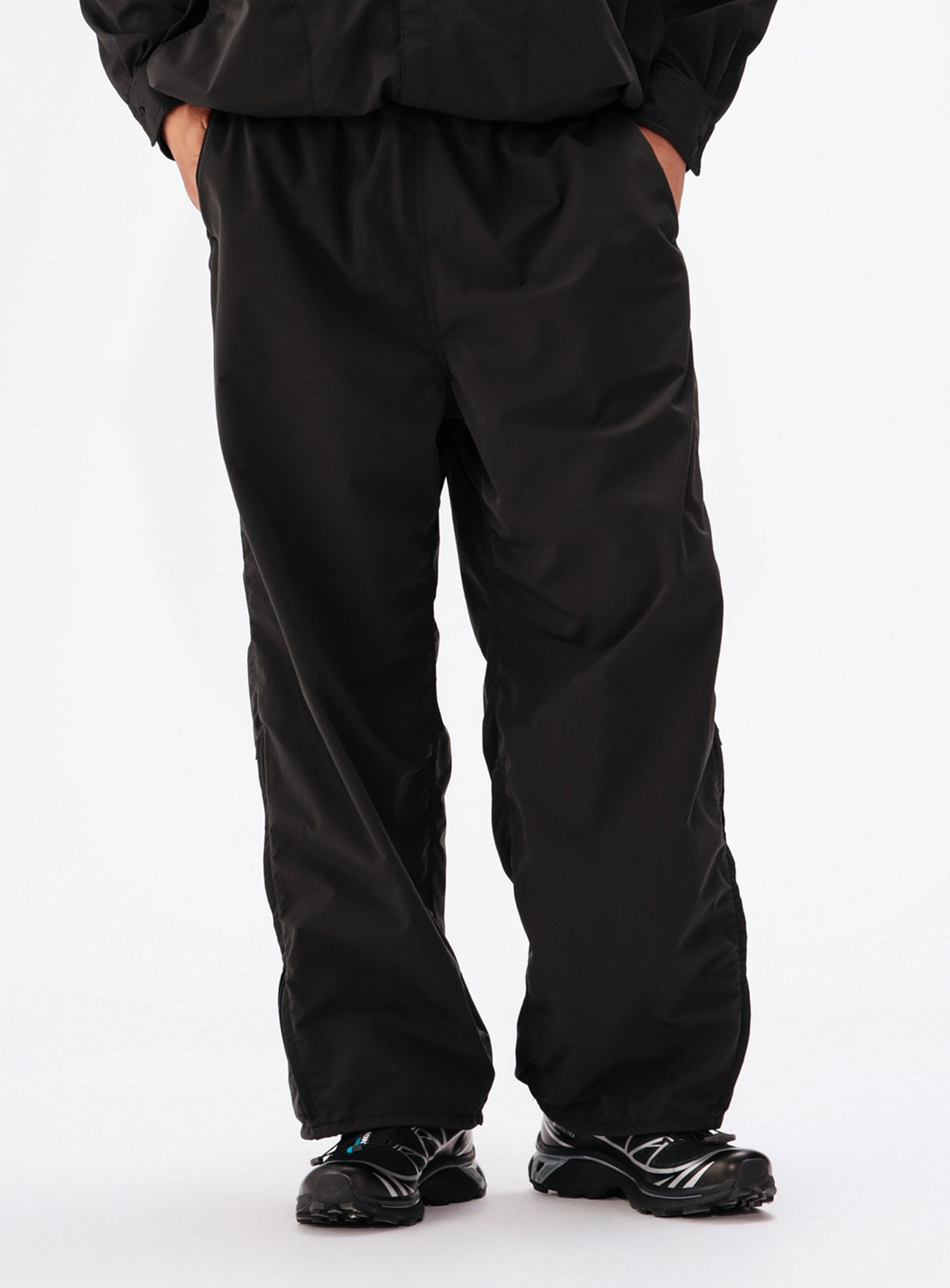 BEAMS Technical 2-Way Adjustable Easy Pants in black, featuring a wide straight-leg fit, stretch double-weave fabric, elastic waistband, and pockets, worn with black athletic sneakers.