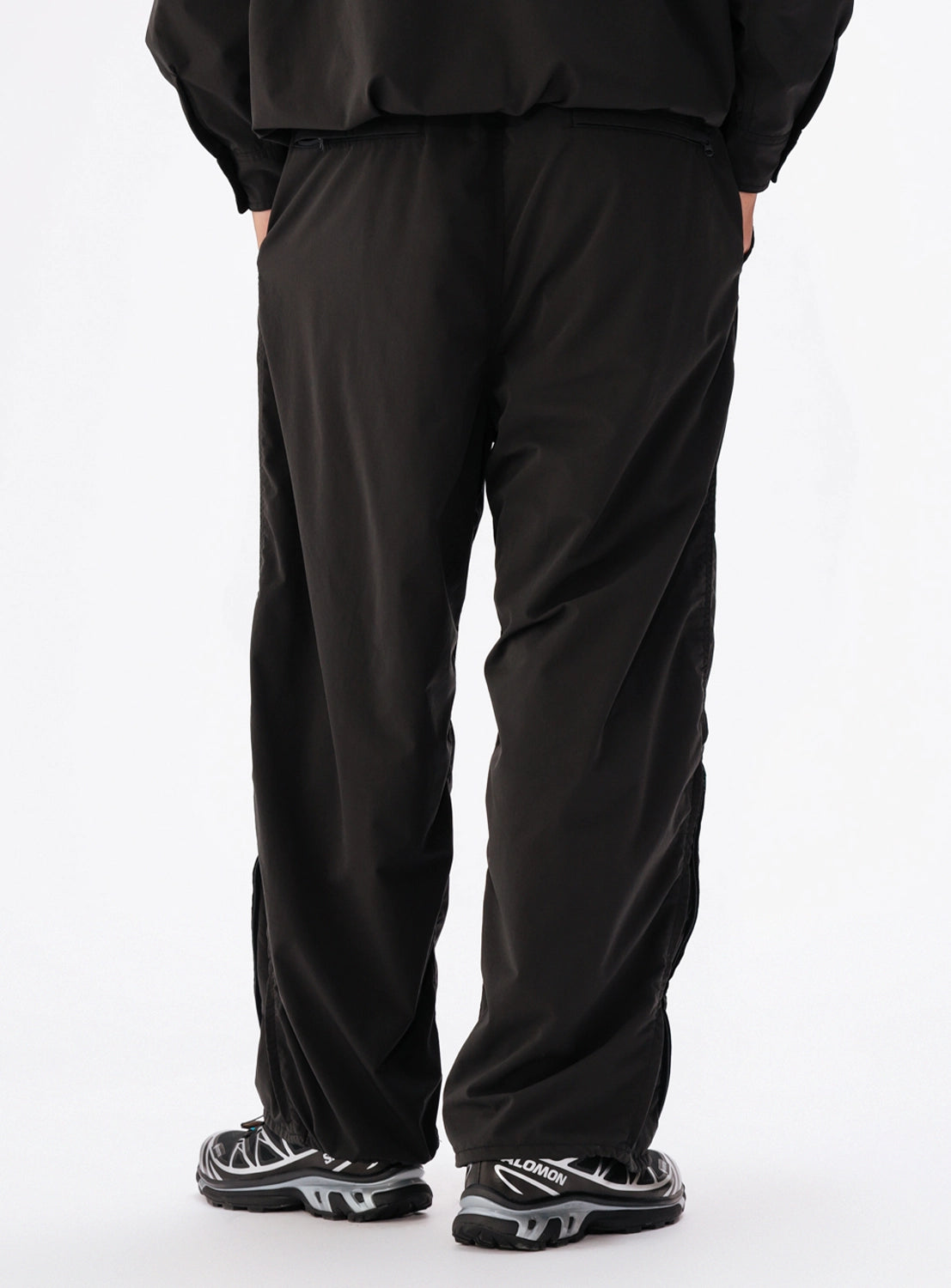 Back view of a person wearing black BEAMS Technical 2-Way Adjustable Easy Pants and black and silver athletic sneakers.