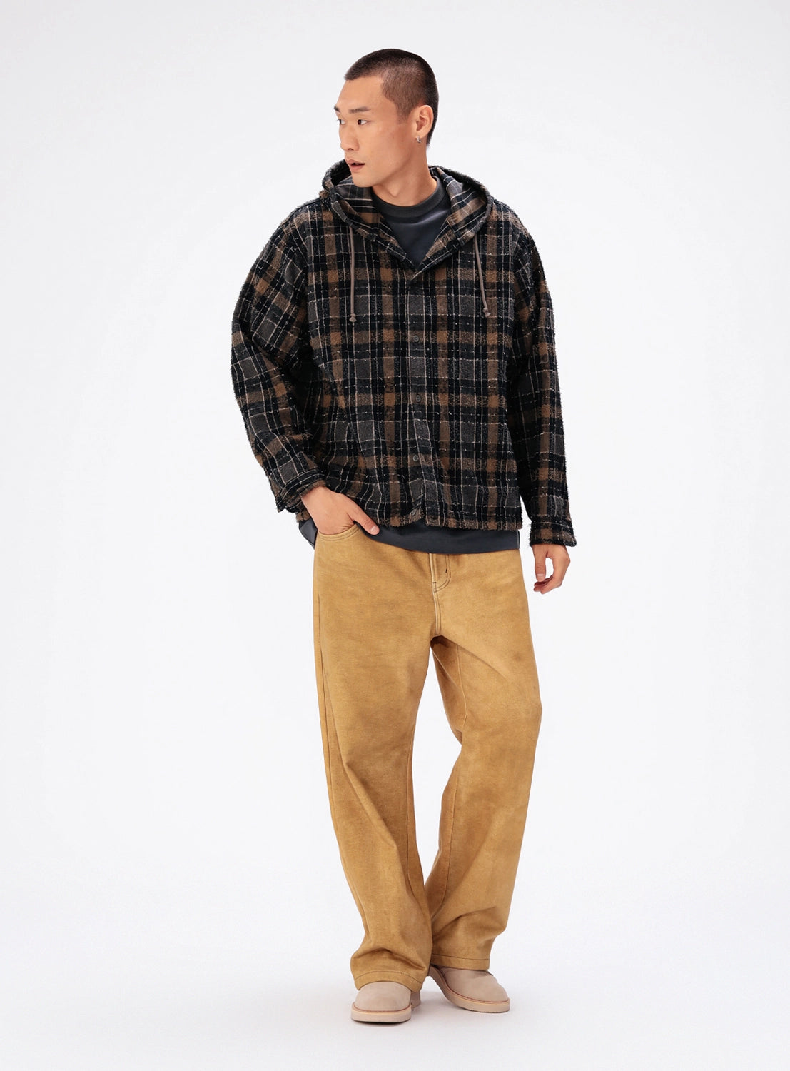 A model wears a vintage-inspired black and brown plaid BEAMS Bouclé Flannel Hooded Shirt over a dark gray t-shirt, paired with tan wide-leg trousers and light-colored shoes.