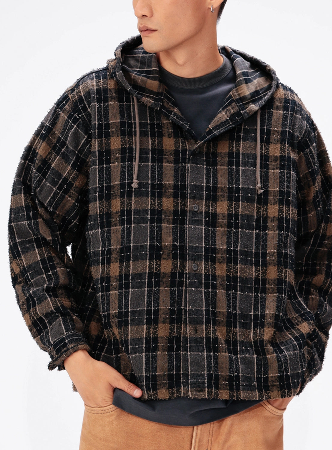 A person wears a BEAMS Bouclé Flannel Hooded Shirt in a vintage-inspired brown and black plaid with frayed edges over a dark gray shirt.
