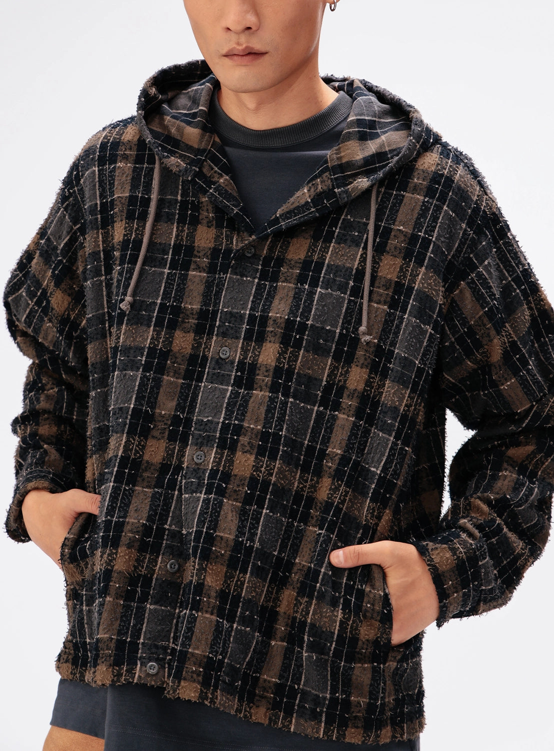 A person wearing a BEAMS Bouclé Flannel Hooded Shirt in a vintage-inspired brown and black plaid pattern with front pockets.
