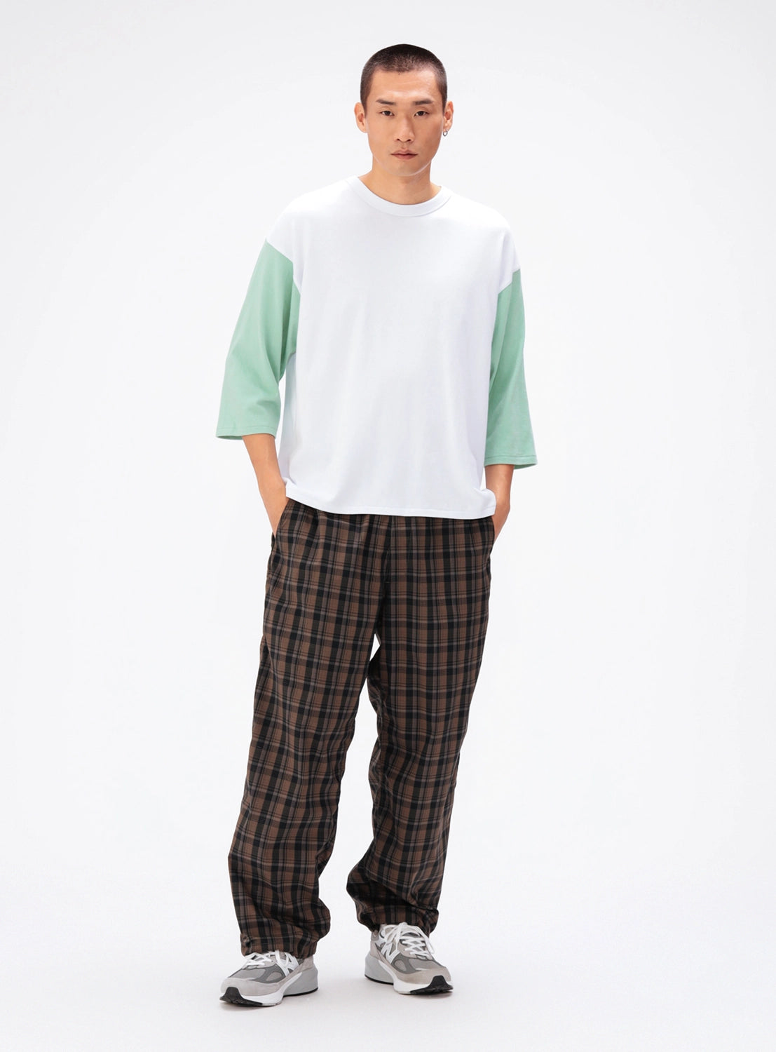 A man wearing a BEAMS Baseball 9/10 Sleeve T-Shirt with mint green three-quarter sleeves, brown plaid trousers, and grey sneakers.