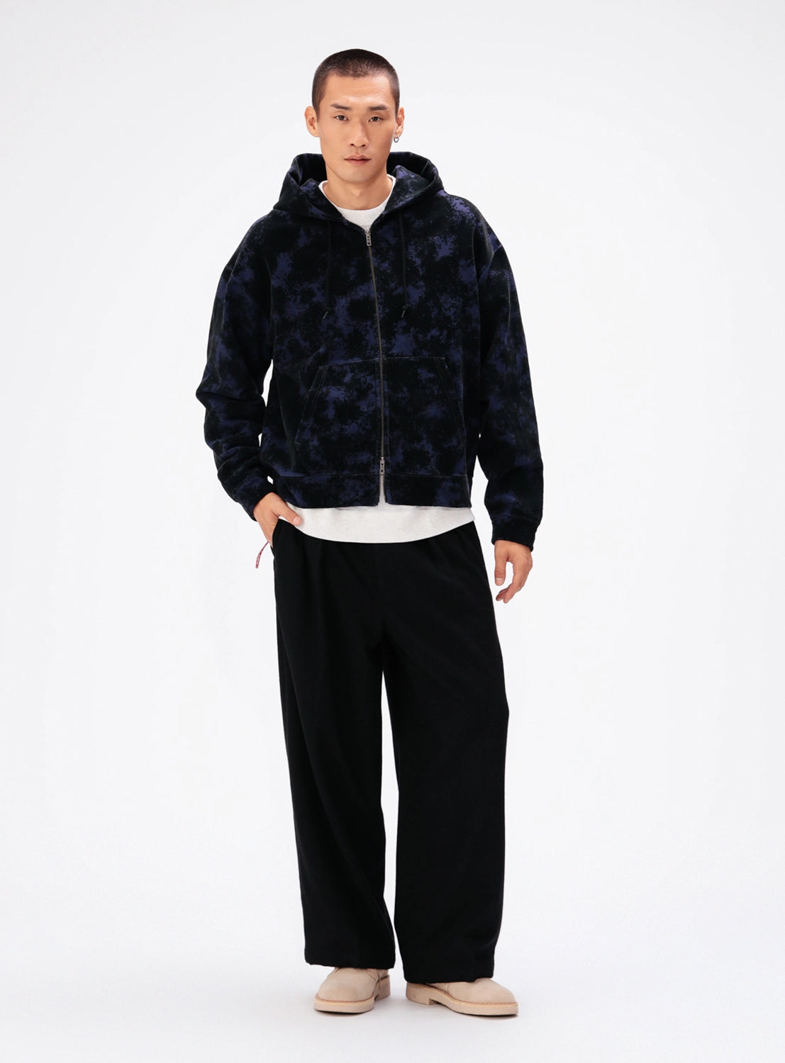 A person wearing a BEAMS Flocked Planet Motif Full-Zip Hoodie in dark blue with a textured planet print, a white t-shirt, and loose-fitting black trousers.