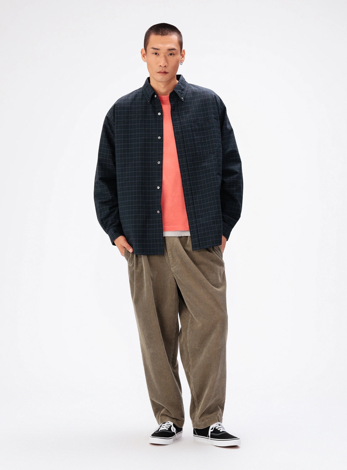 A man wears a BEAMS Heavy Oxford Button-Down Shirt over a coral t-shirt, paired with relaxed-fit olive trousers and black sneakers.