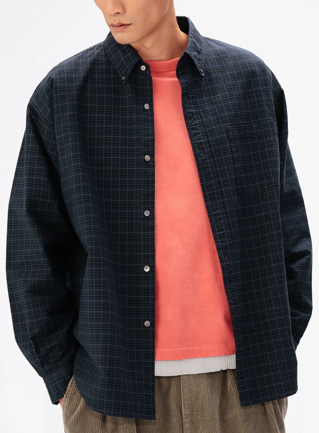 A person wearing a BEAMS Heavy Oxford Button-Down shirt with a dark grid pattern over a coral t-shirt and tan trousers.
