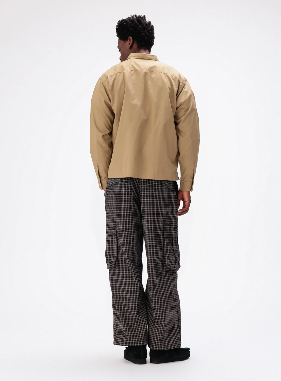 A person seen from behind, wearing a tan button-down shirt and BEAMS Pattern 6-Pocket Pants, which are relaxed fit, dark checkered cargo pants with side pockets.