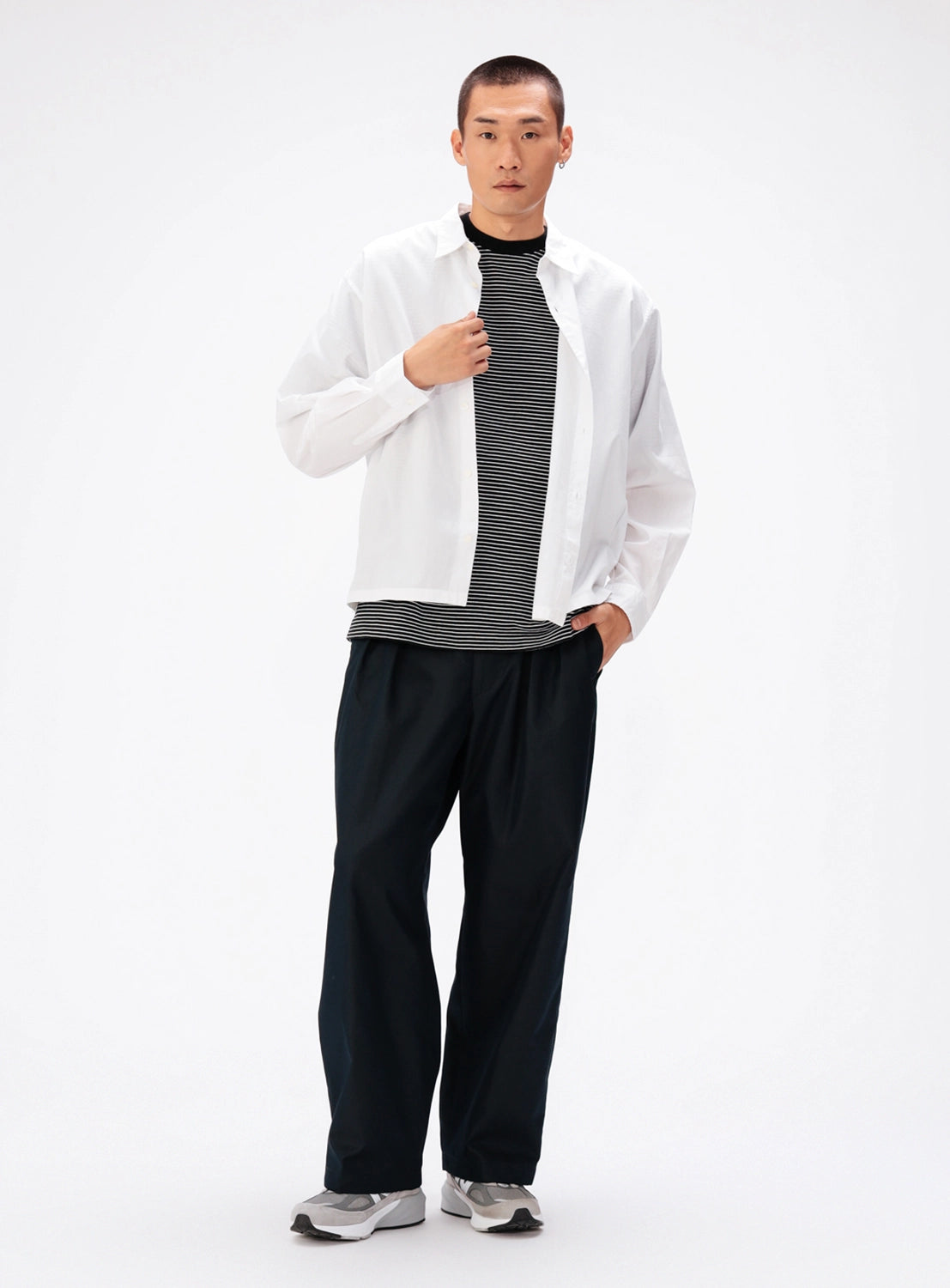 A person wearing an unbuttoned white shirt over a black and white striped shirt, loose-fitting BEAMS Chambray Chino Pants, and grey sneakers.