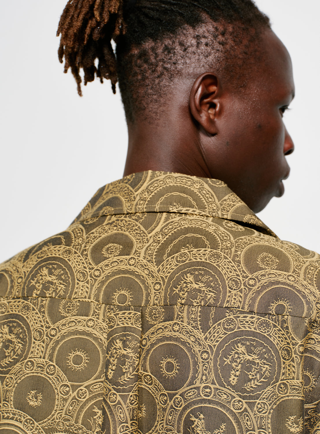 Detailed collar view of a model wearing a brown and yellow Italian patterned, collared button down shirt. 