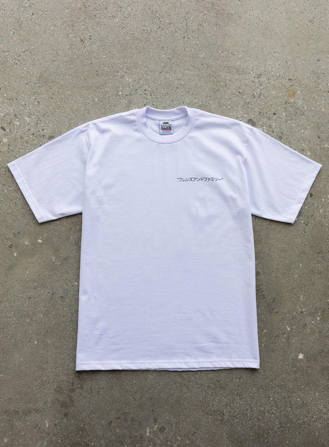 The J. BRIAN x BEAMS TEE from BEAMS AMERICA is a limited edition short-sleeve T-shirt, showcased laid flat on a concrete surface. It features original artwork and subtle Japanese text printed on the left chest, offering a unique and stylish anniversary model design.