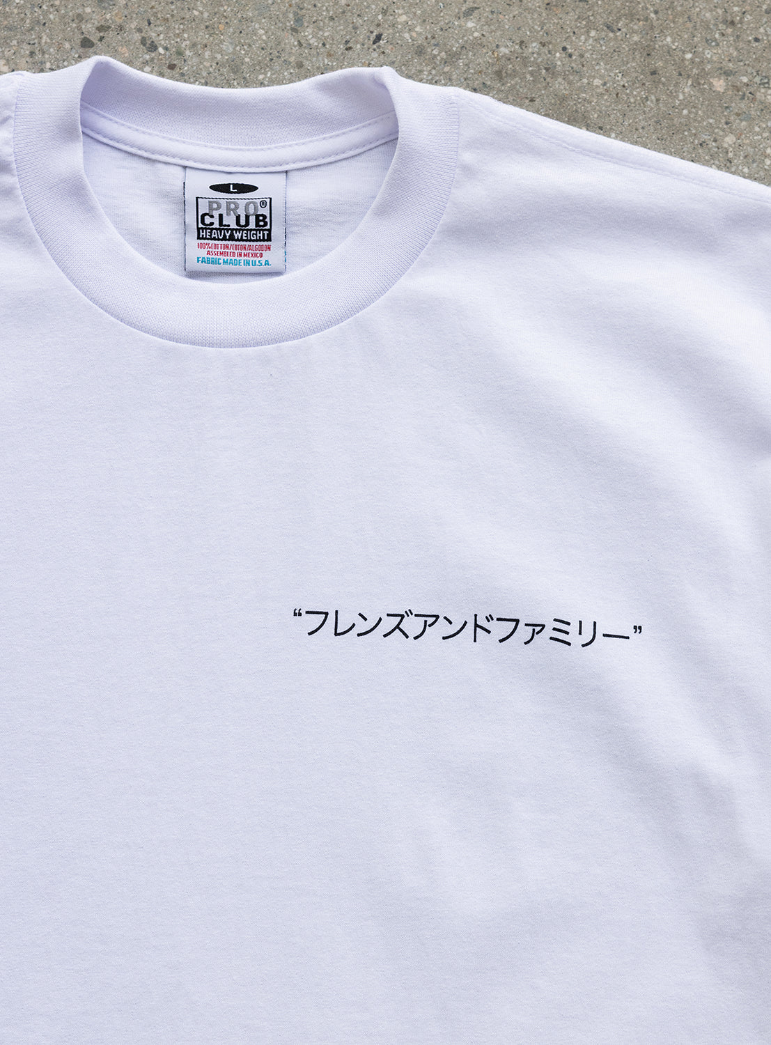 A white, limited edition J. BRIAN x BEAMS TEE by BEAMS AMERICA featuring Japanese katakana text “フレンズアンドファミリー” on the front. The CLUB HEAVYWEIGHT label is visible, and this special anniversary model showcases original artwork, displayed lying on a textured surface.