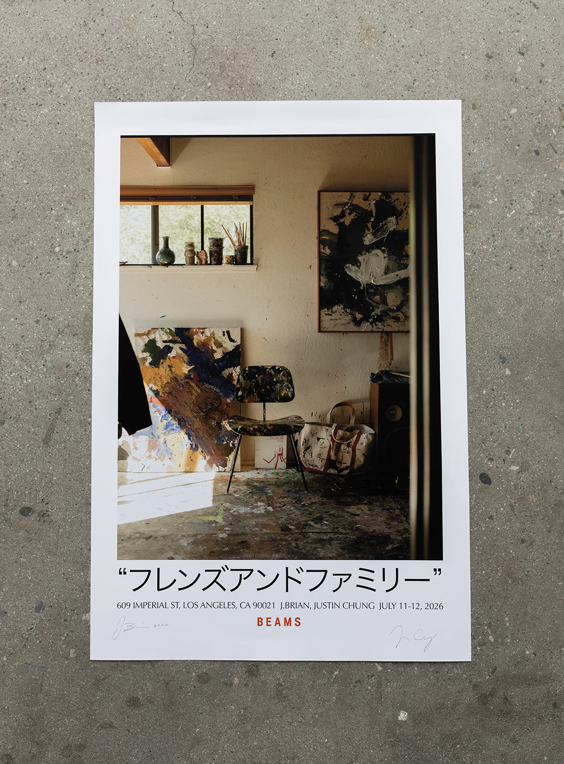 A J. BRIAN x BEAMS POSTER 2 by BEAMS AMERICA is displayed on a speckled concrete floor, featuring an artist’s studio scene with a chair, canvas, and art supplies—including what looks like an exclusive 50th-anniversary sneaker amid original artwork. Japanese text and event details appear at the bottom.