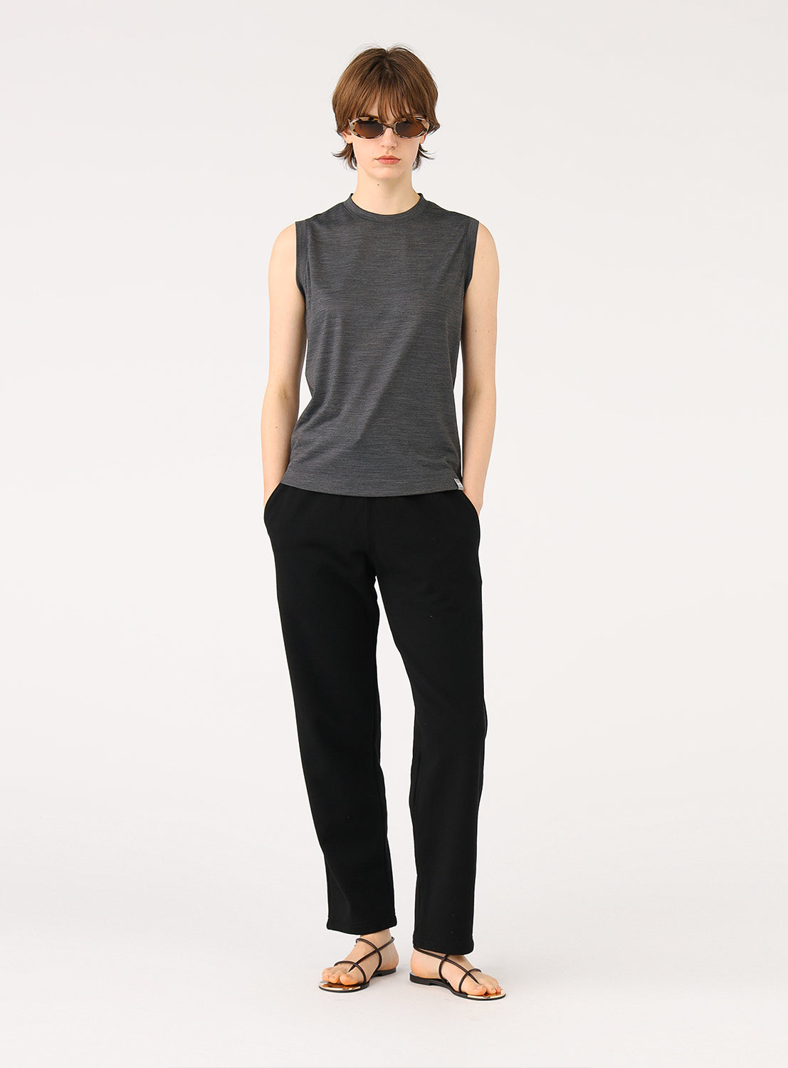 Full body shot of a model wearing the dark grey sleeveless top, styled with black pants and sandals.