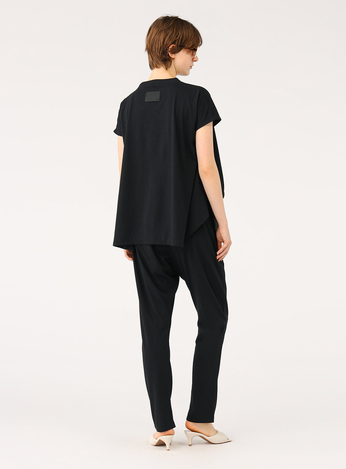 Back view of a model in the black jumpsuit, showing the oversized top and the back of the tapered pants.