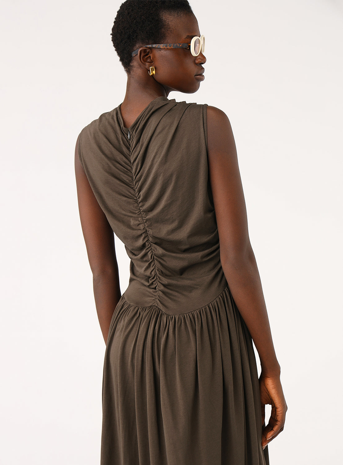 Back view of the model in the brown dress, highlighting the draping and ruching details on the bodice and waist.