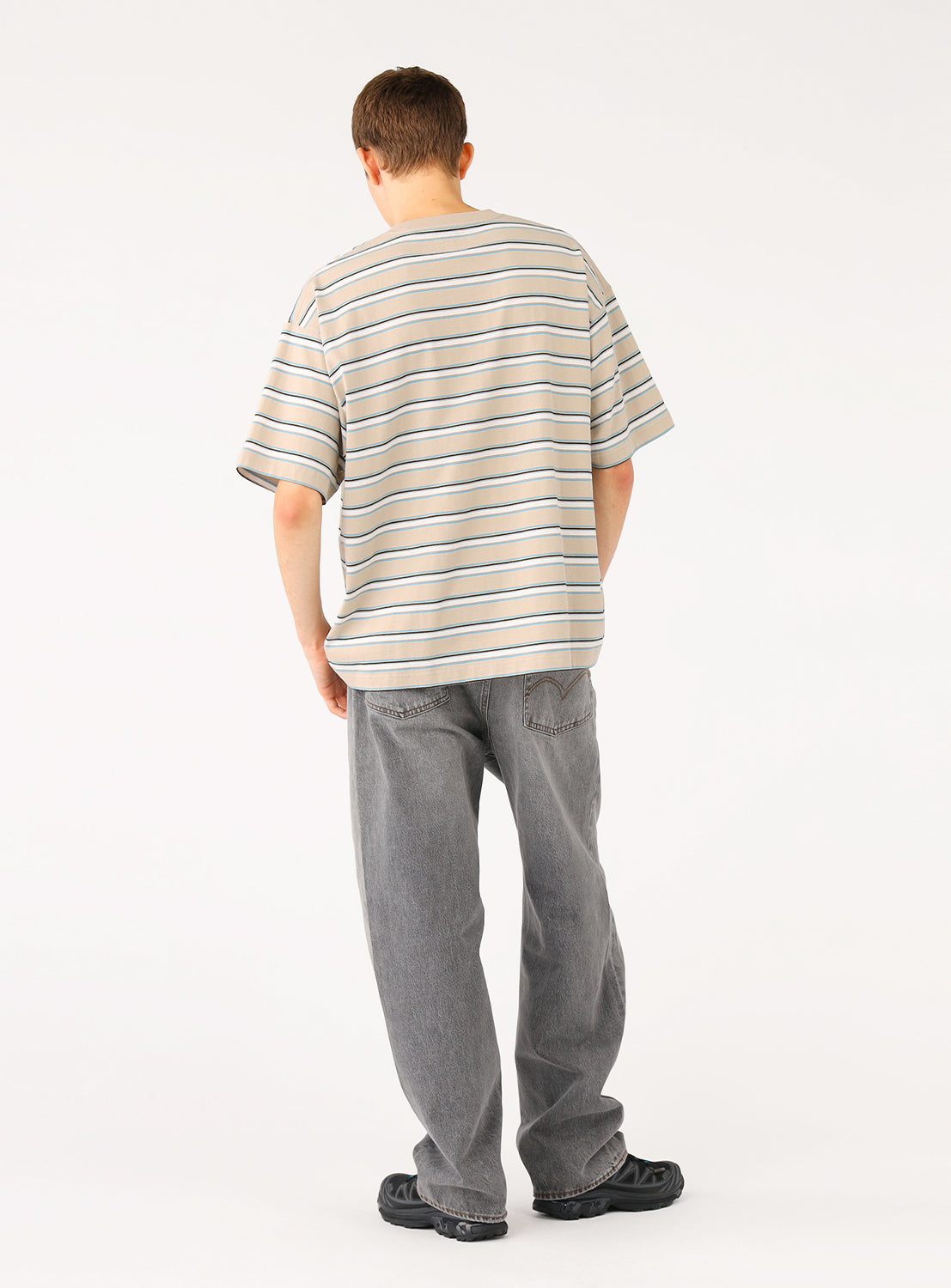 Back view of a model in the beige striped t-shirt, showcasing the relaxed fit from behind.
