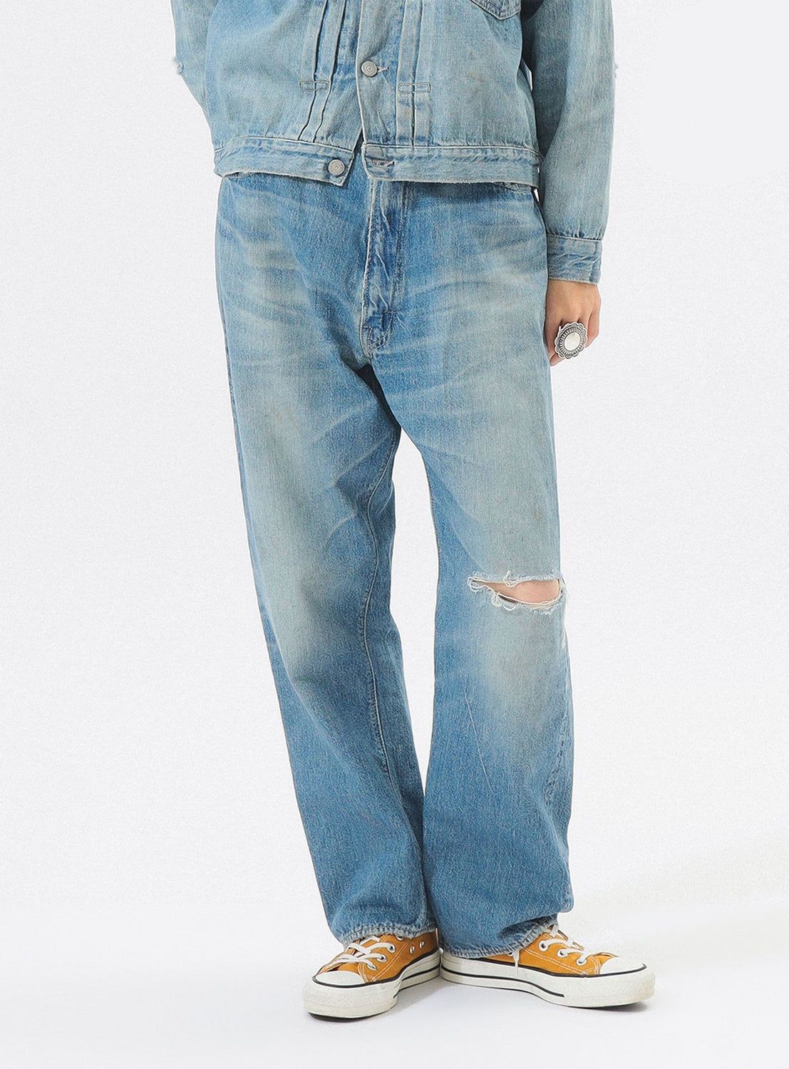 Person wearing a light blue denim jacket and jeans with a white background