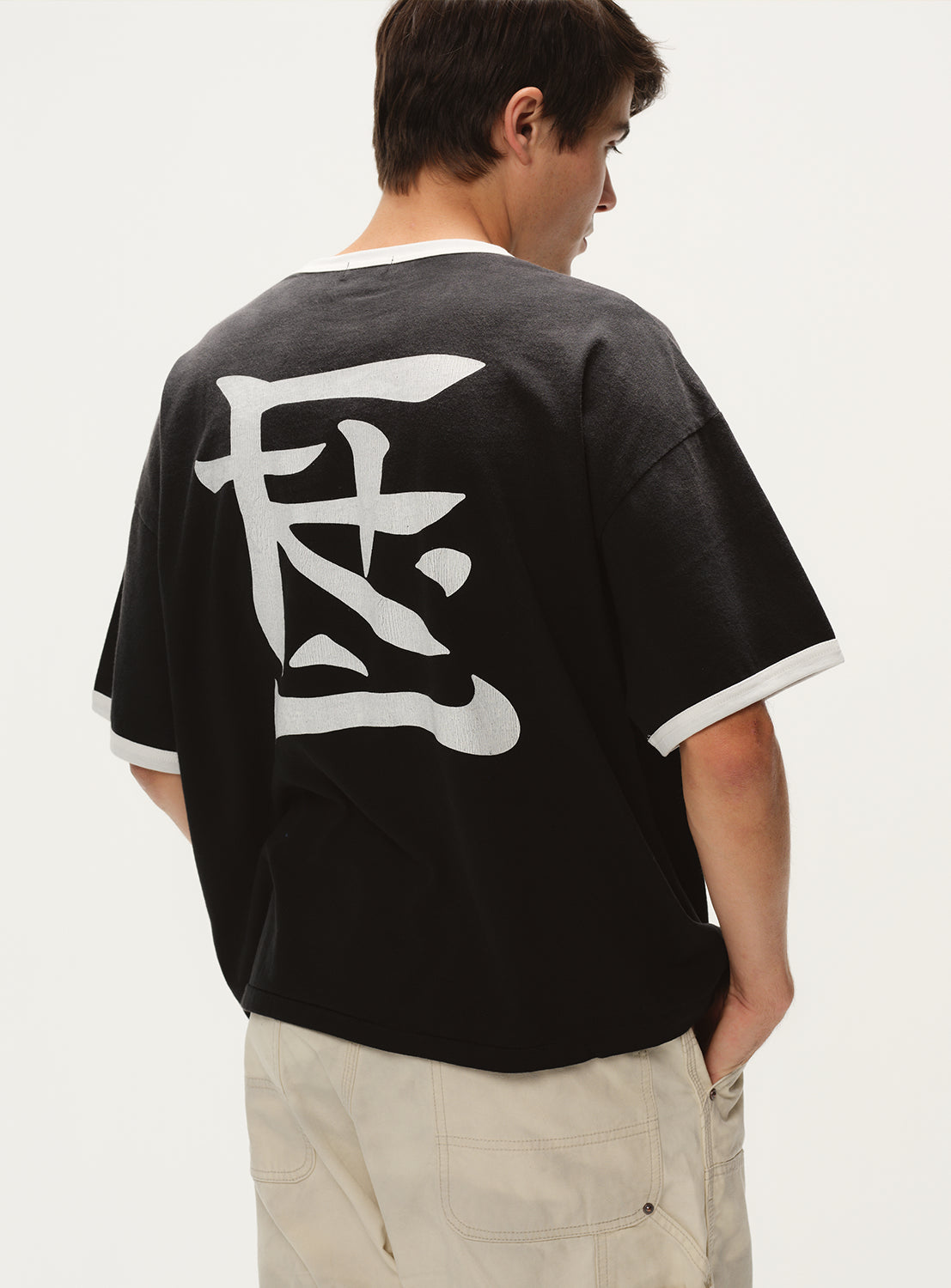 Model wearing a dark grey t-shirt, back view, showcasing the white stylized graphic print on the upper back.