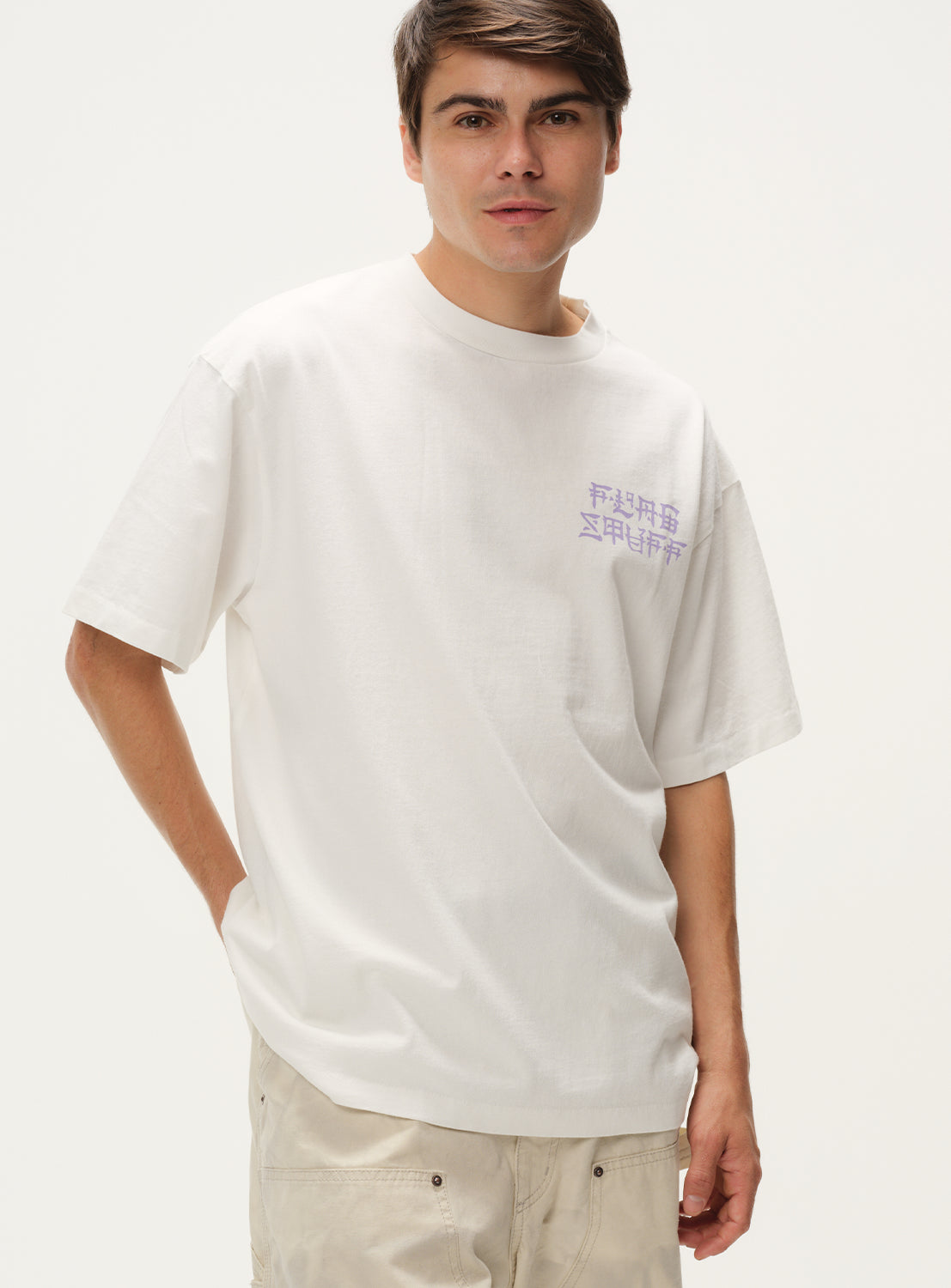 Model wearing a white t-shirt with purple text graphic and khaki pants, front view, displaying casual fit.