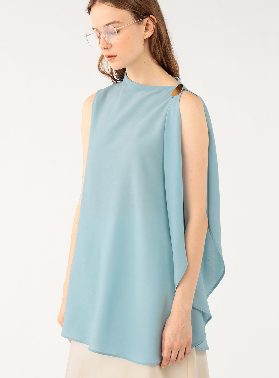Woman wearing a light blue sleeveless top showcasing the detail of the draping on the side. 
