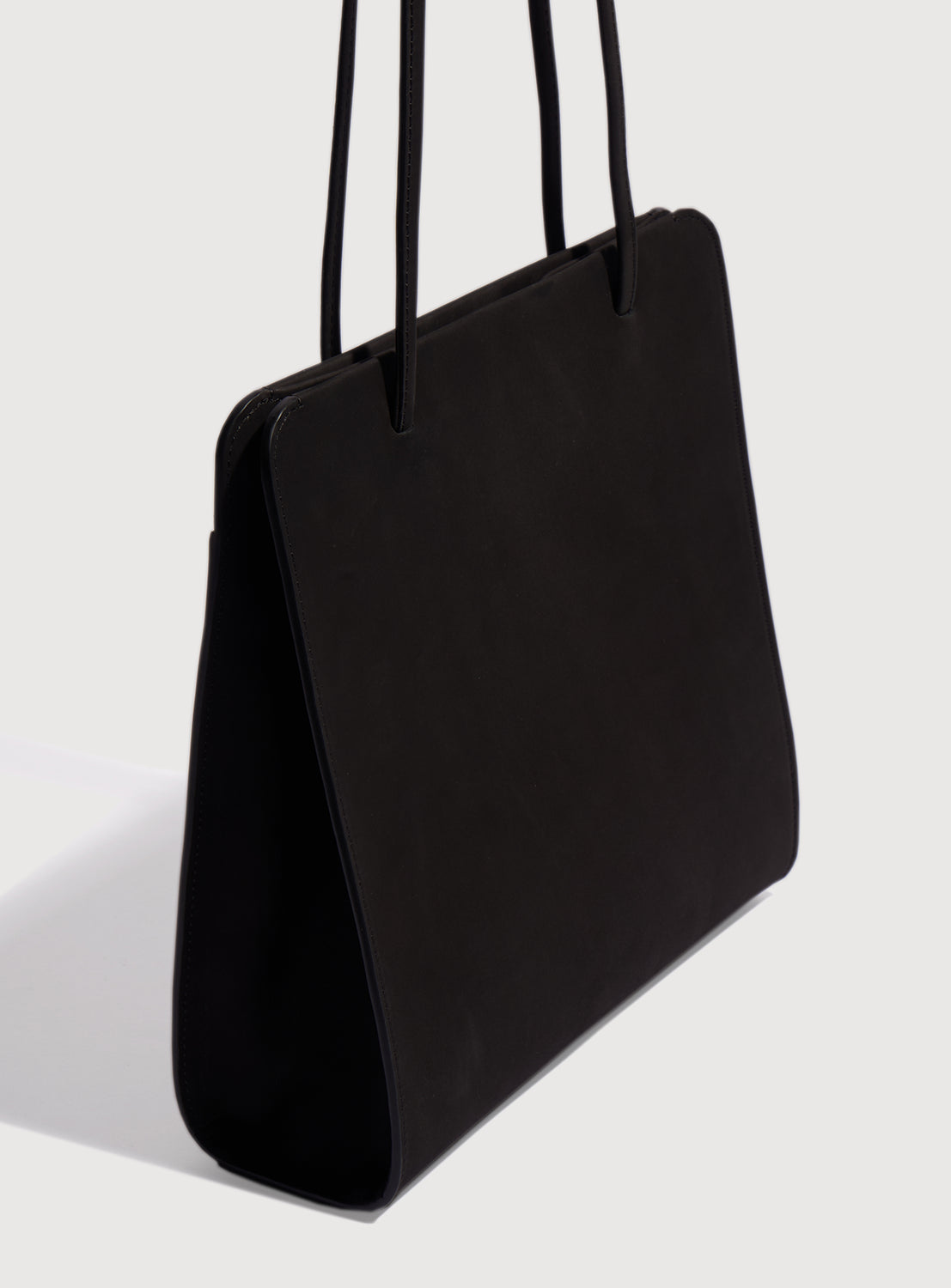 Side quarter view of a black square  handbag with long, ribbon-like straps.