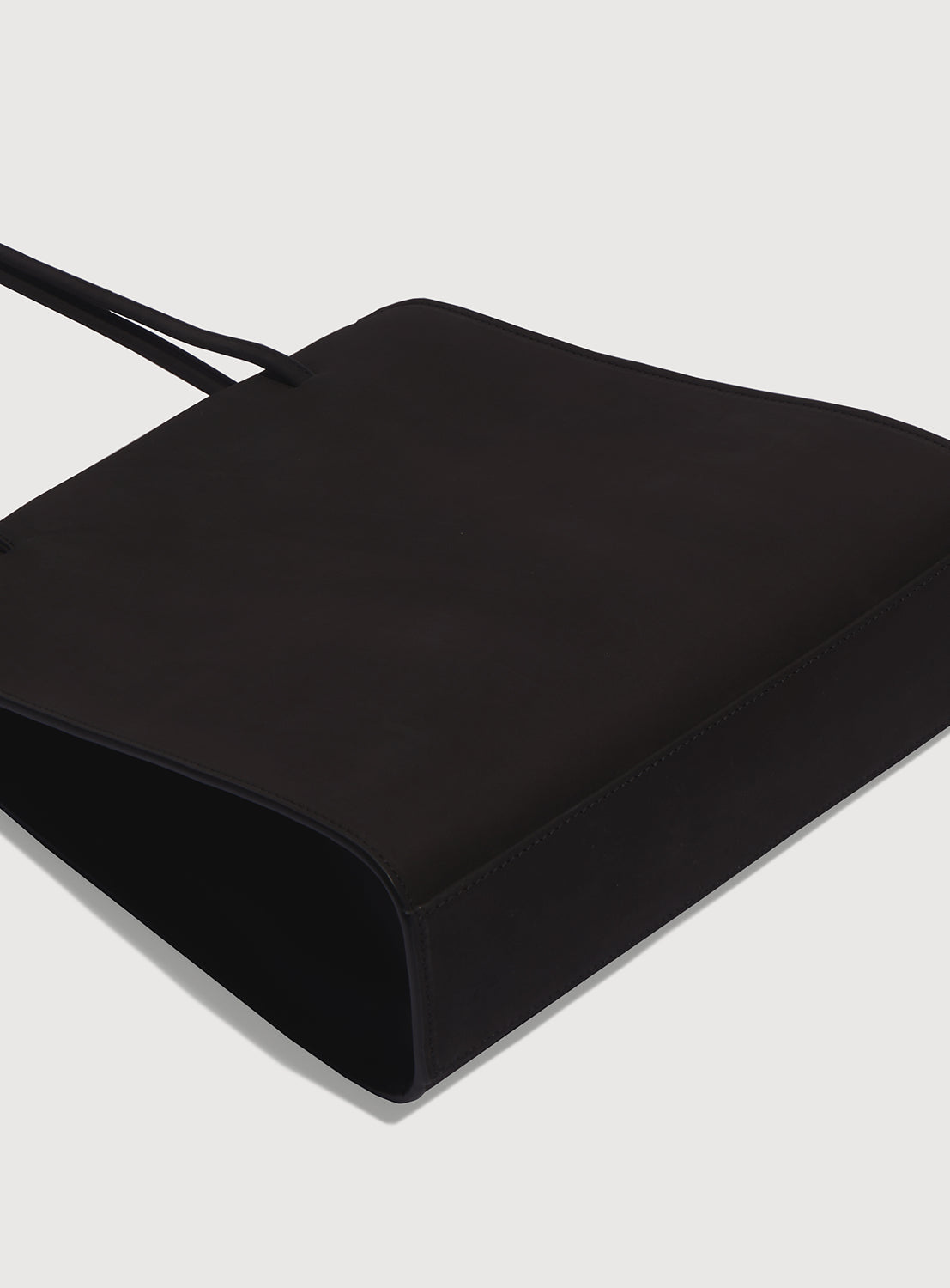 Bottom view black square handbag with long, ribbon-like straps.