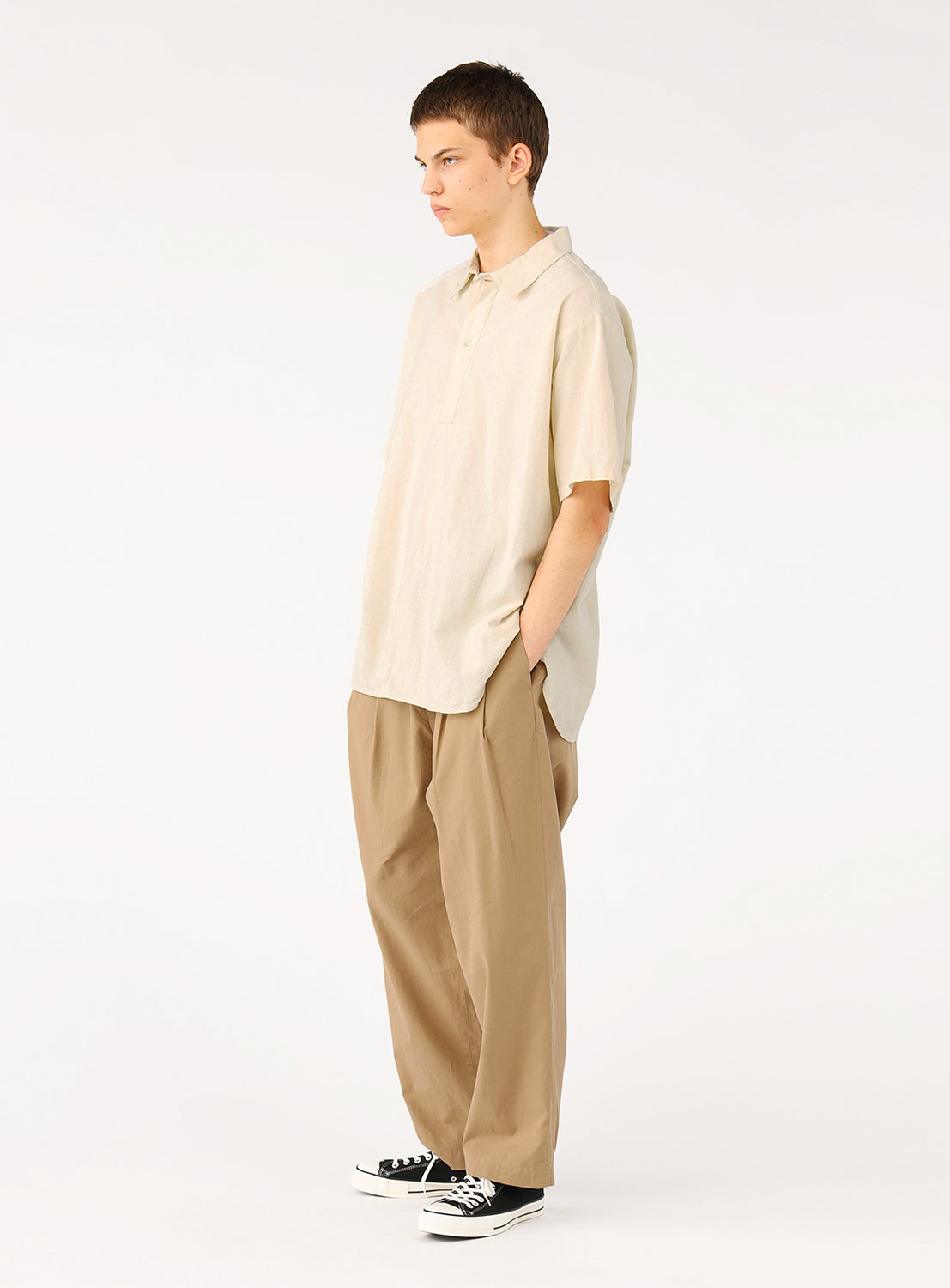 Model wearing a natural (beige cream) military pullover shirt, side view, emphasizing the relaxed fit and drop shoulders.