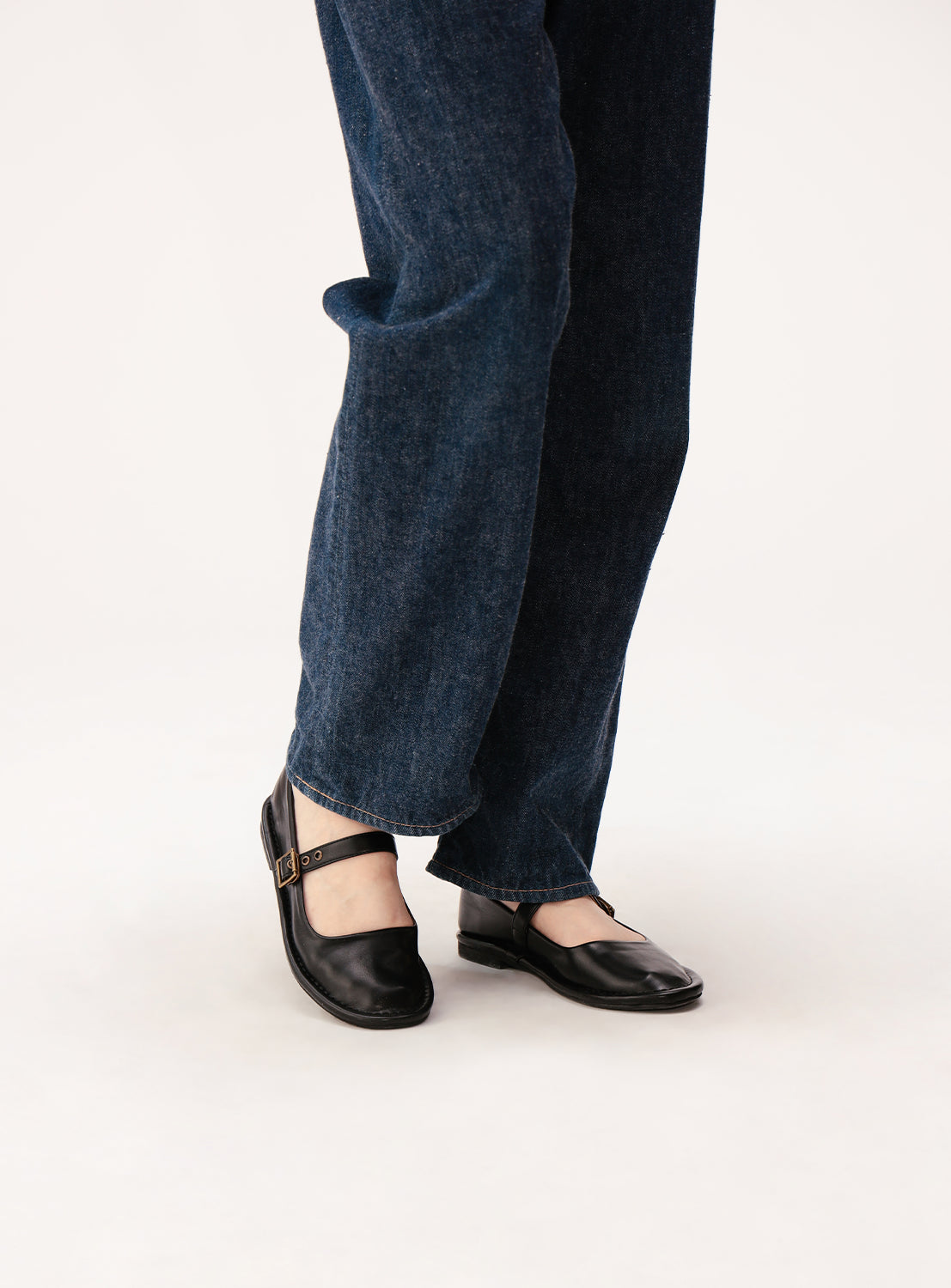 A person is wearing dark blue jeans paired with BEAMS BOY Mary Jane Shoes featuring a sleek buckle, standing on a white background—a classic ensemble that highlights feminine balance and is ideal for Spring/Summer 2026.