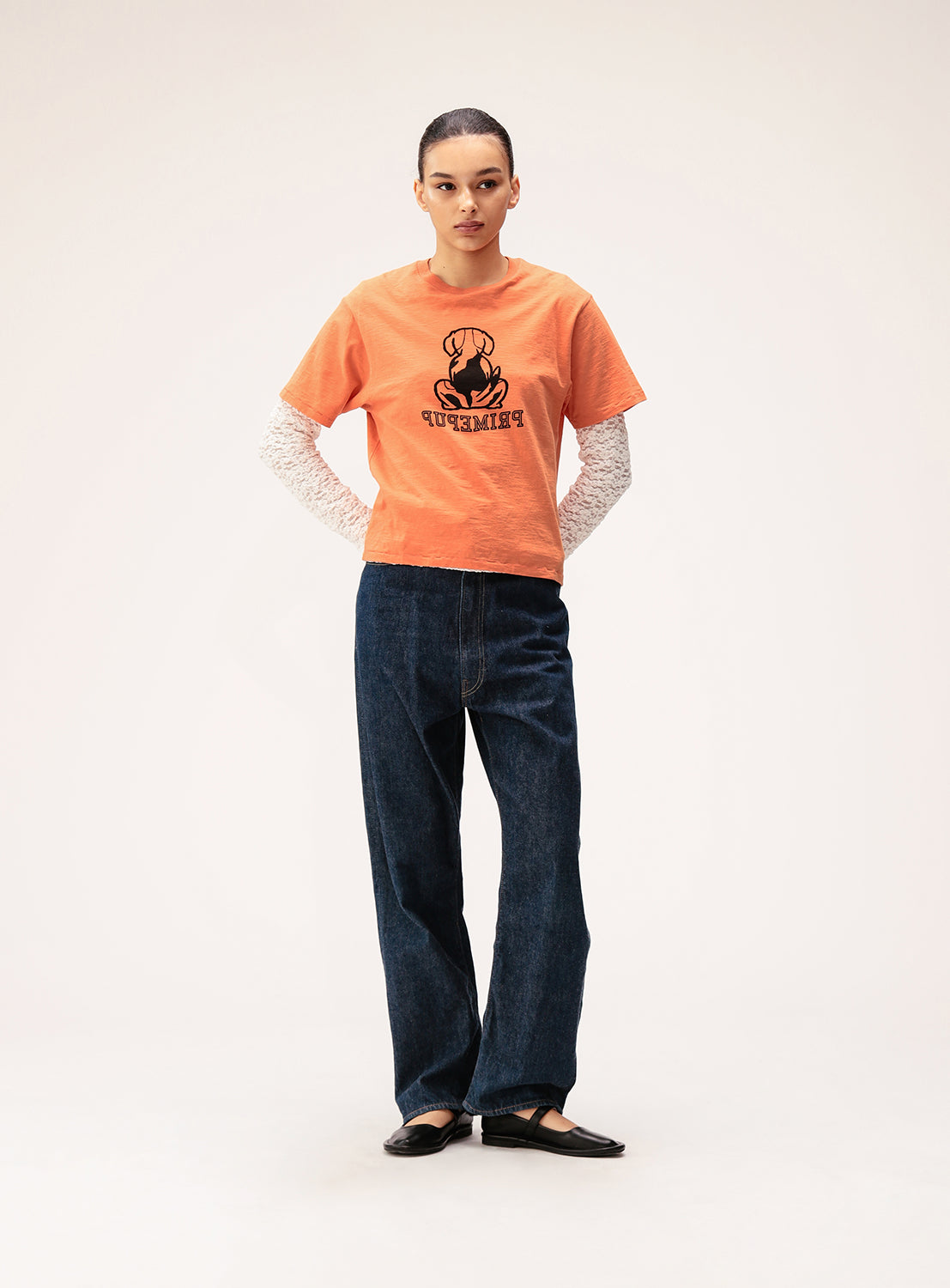 A person stands facing forward in an orange graphic t-shirt with "PINHEAD" text, layered over a white long sleeve top, paired with dark jeans and BEAMS BOY Mary Jane Shoes for a touch of feminine balance, set against a plain light background—creating the perfect look for Spring/Summer 2026.