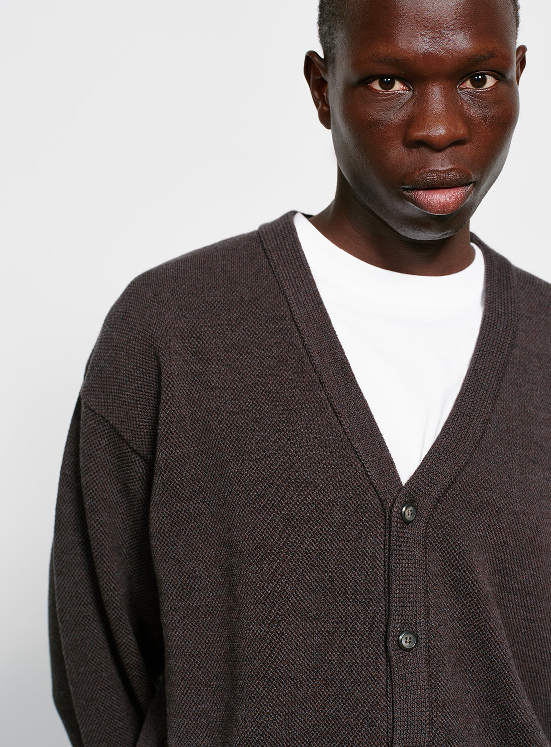 Close up of a model wearing a gray button down cardigan with pockets on a white background.