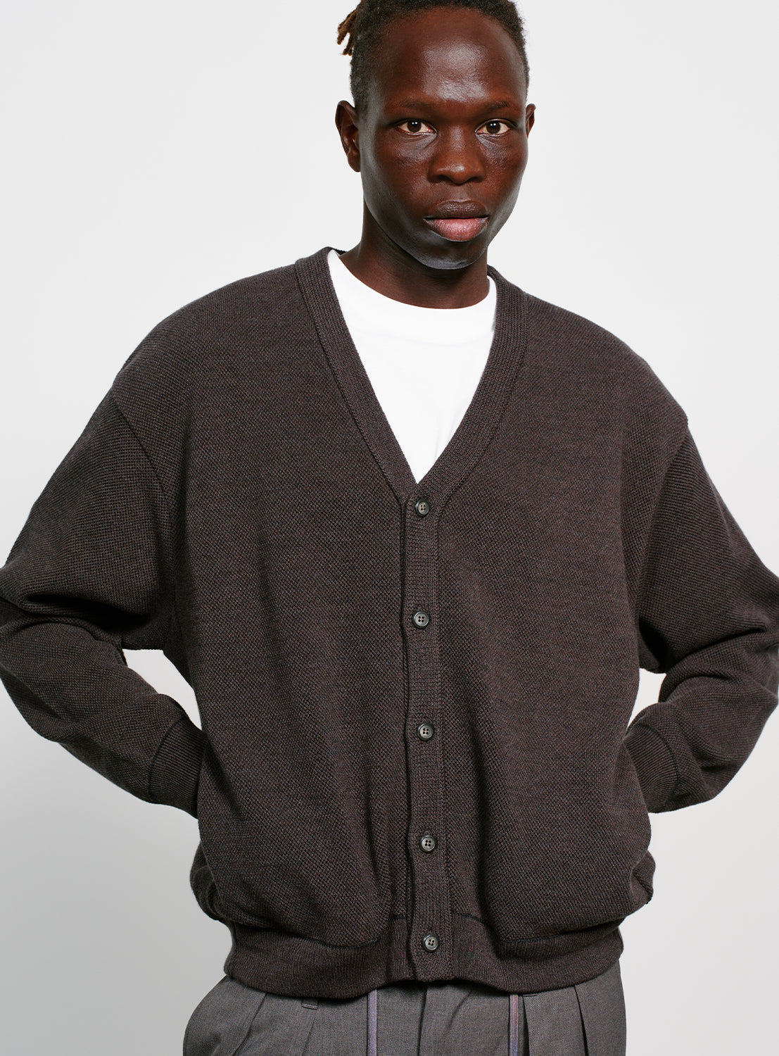 Model wearing a gray button down cardigan with pockets on a white background.