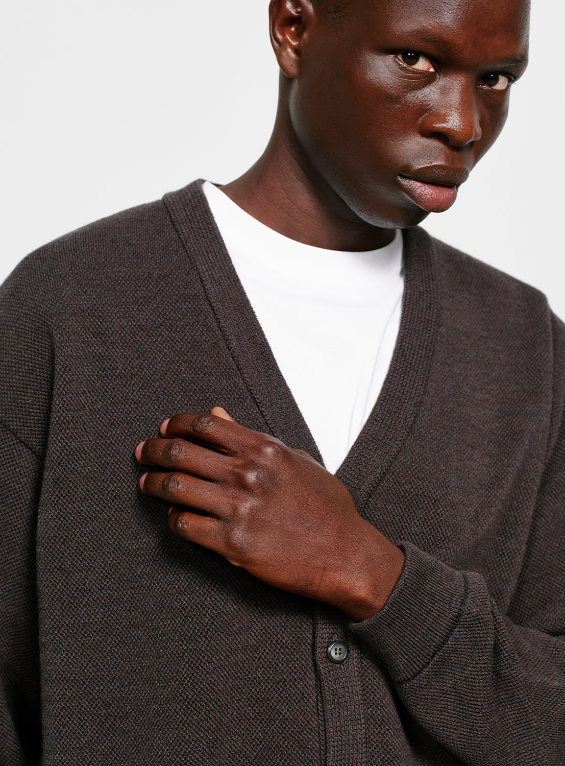 Close up of a model wearing a gray button down cardigan with pockets on a white background.