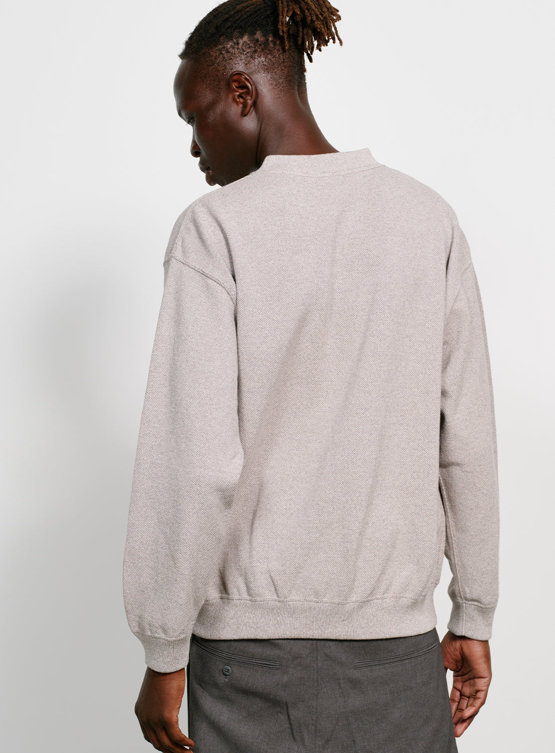 Back of a model wearing a grey crew neck sweater.