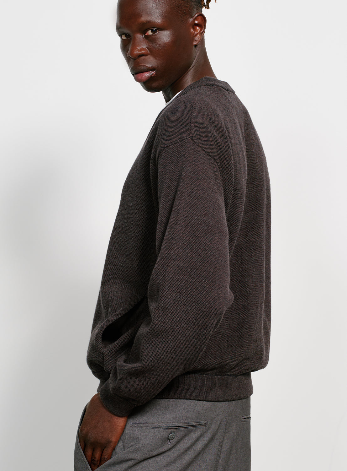 Back of a model wearing a gray button down cardigan with pockets on a white background.