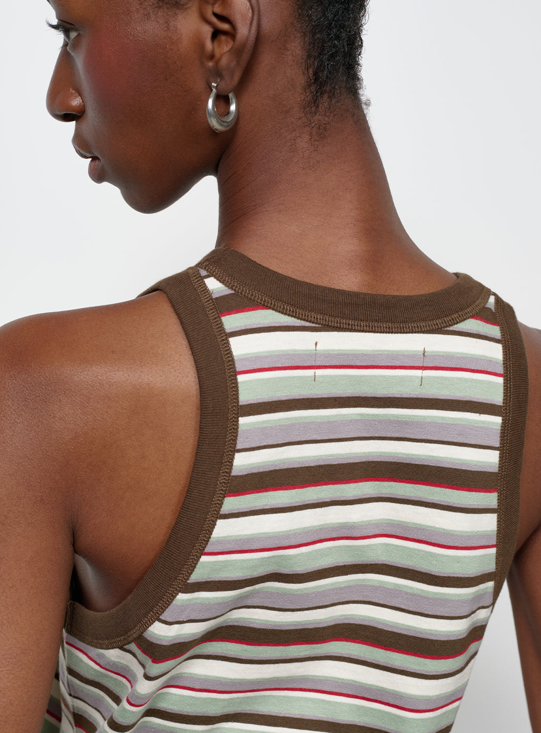 Close up view of a model wearing a multi-colored striped tank top with brown trim.