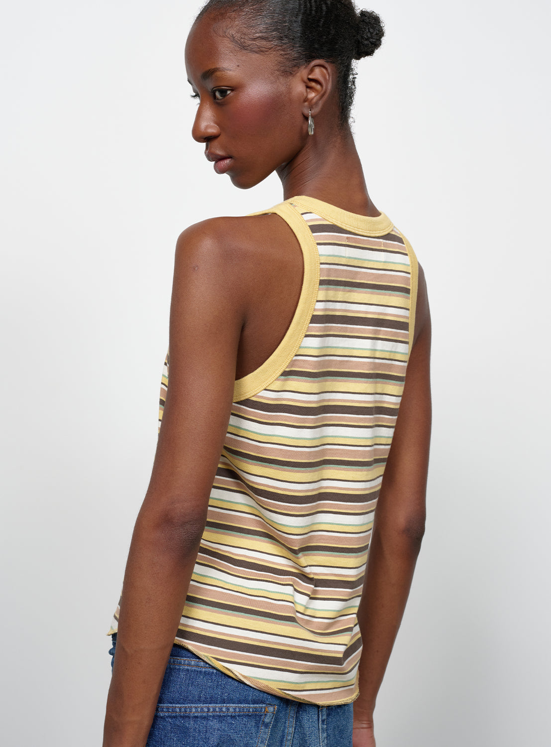 Back view of a model wearing a yellow shirt with, brown, white, pink and baby blue stripes. 