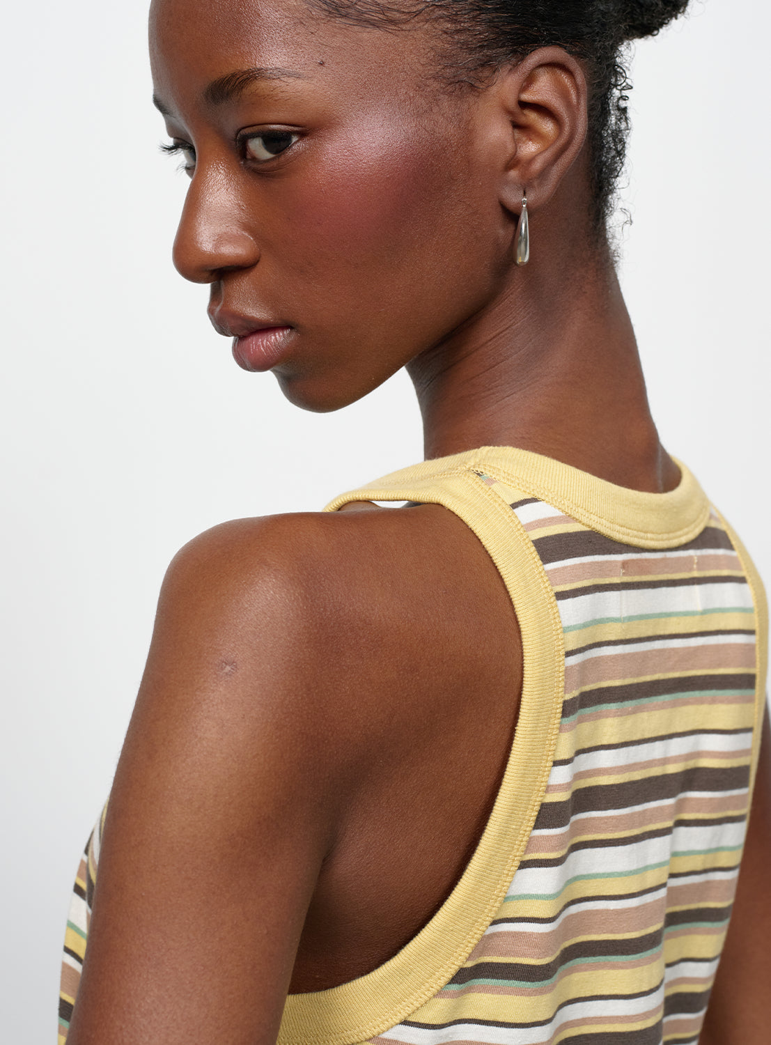 Close up of a model wearing a yellow shirt with, brown, white, pink and baby blue stripes. 
