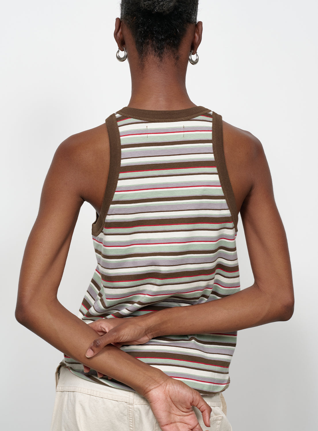 Back view of a model wearing a multi-colored striped tank top with brown trim.