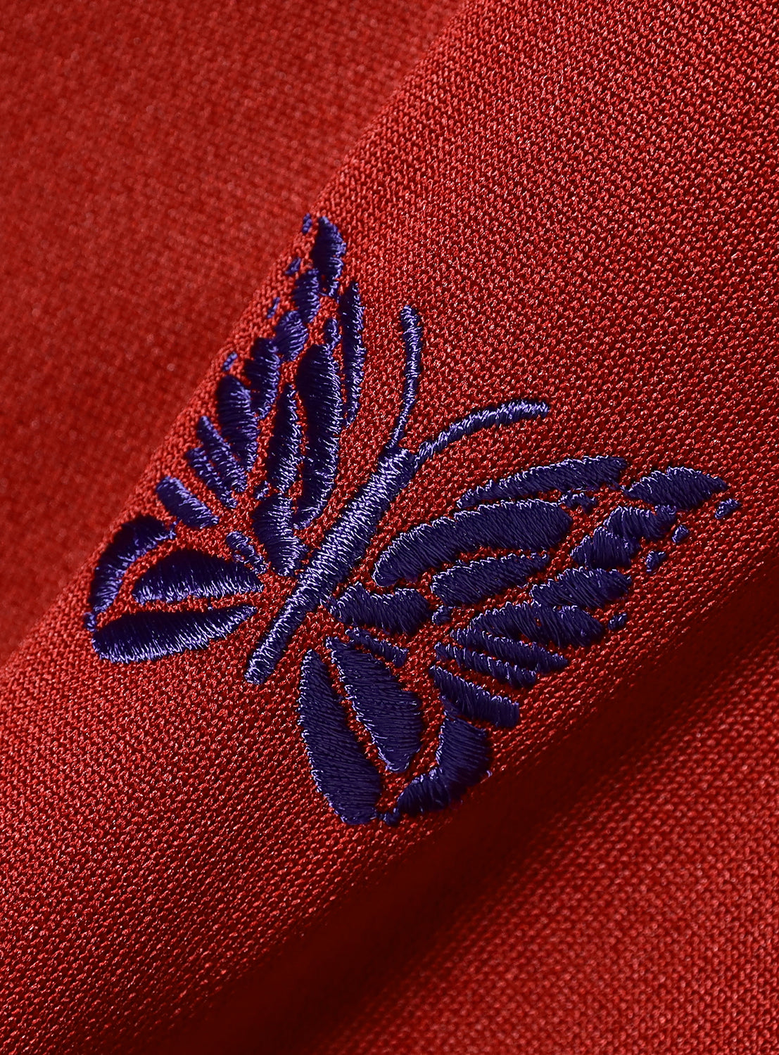 Close-up of a red fabric with a purple embroidered butterfly design.