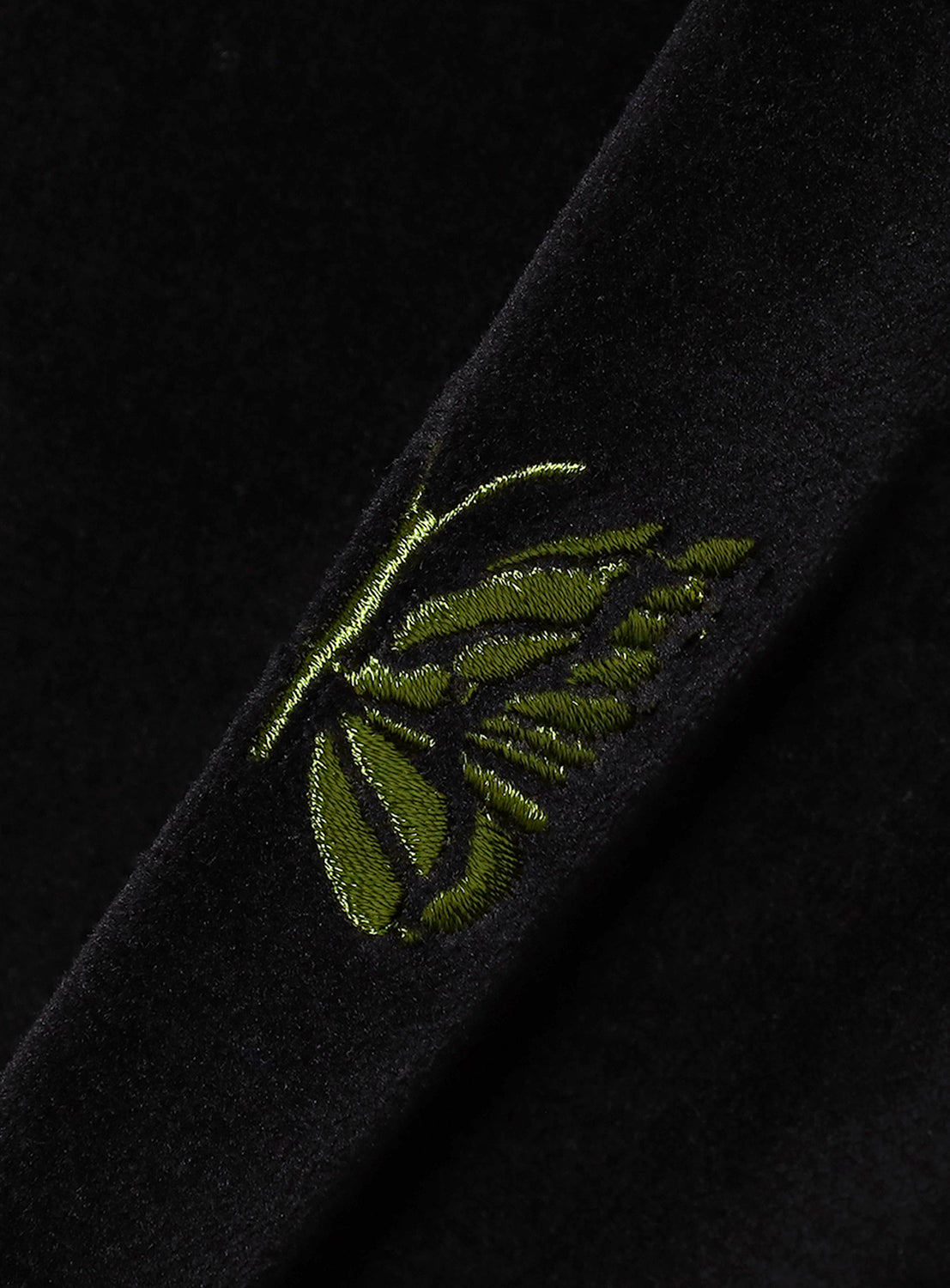 Close-up of a black fabric with green embroidered butterfly design.