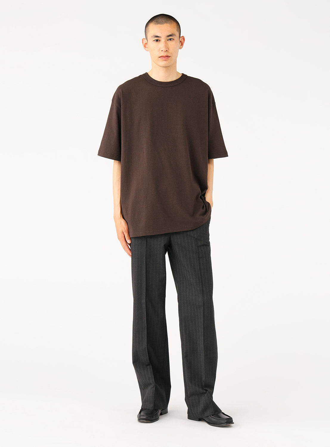 Front view of a man modeling a comfortable dark brown oversized t-shirt, paired with relaxed fit black trousers.